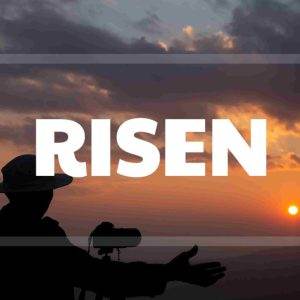 Person silhouetted against a dramatic sunrise with arms raised and the word "RISEN" overlayed