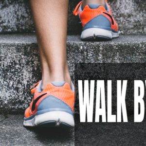 Close-up of a person walking up concrete steps in orange sneakers with the text "Walk by Faith".