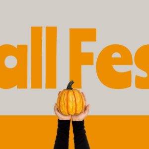 Hands holding a small pumpkin in front of an orange Fall Fest sign.